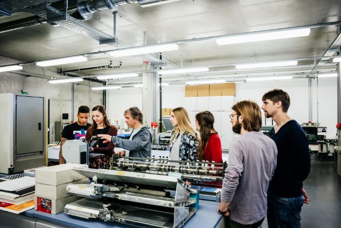 Printing press with students surrounding it with a professor teaching them how to use it. Educator Resources Directory of Schools​